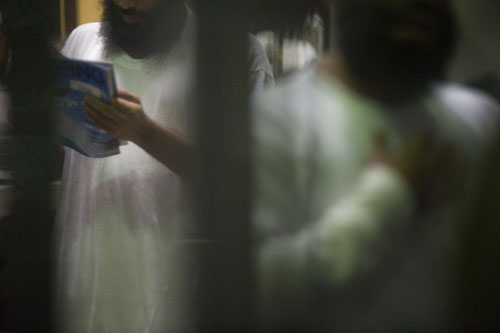 Through a barred enclosure, a detainee can be seen reading a surfing magazine.