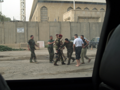 A group of Iraqi soldiers dressed in fatigues scuffle on the street.