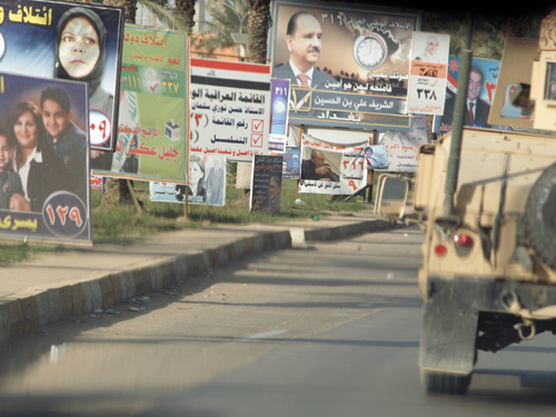 American armored vehicles convoy down abandoned streets and past rows of election posters.
