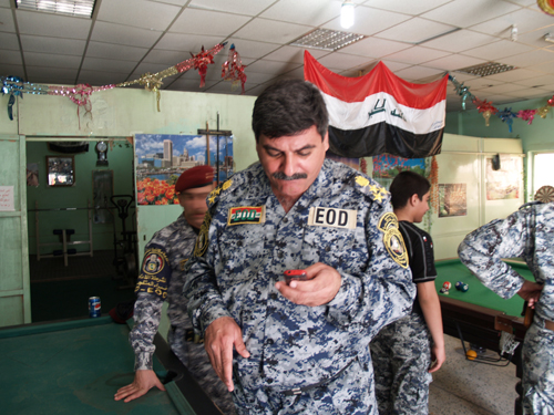An Iraqi officer in uniform watches the screen of his cell phone in the recreation room of the General Counter Explosive Directorate.