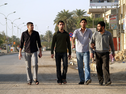 Four smiling men casually walk down the otherwise abandoned streets of Baghdad.
