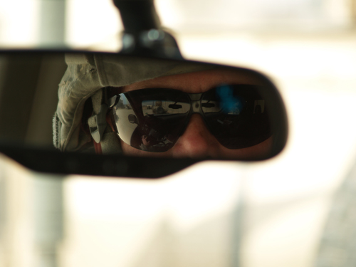 The sunglasses of a soldier are visible in his rearview mirror.