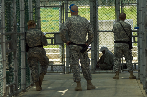 A detainee sits in the outdoor recreation area in Camp 5 watched by three guards.