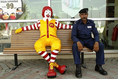 A Pakistani security guard sits on a bench next to a fiberglass statue of Ronald McDonald.