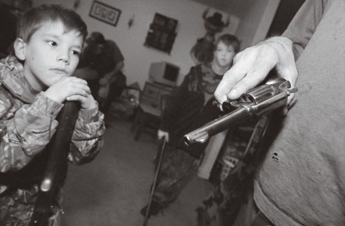 Young Boy Leaning on a Rifle, Gazing at a Handgun