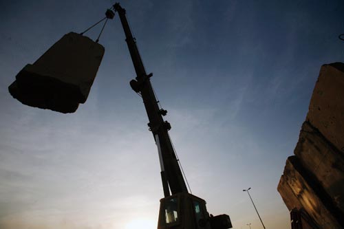 A crane hoists a large concrete wall into the air