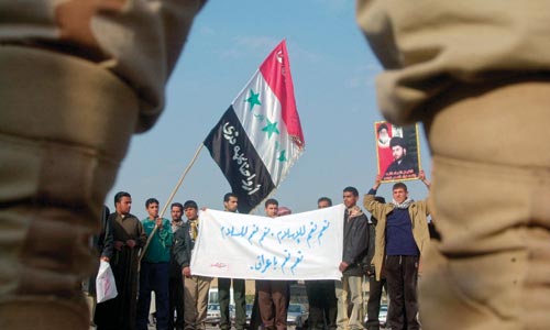 A small group of Iraqi men line a street, holding a banner and an Iraqi flag.