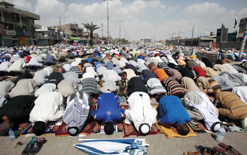 Hundreds of men bow, at prayer, touching their heads to the rugs beneath them. They are outside.