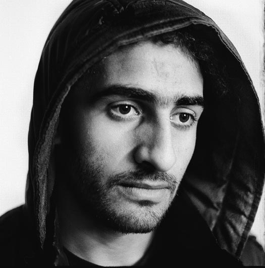 A young man with a light beard and a jacket with the hood raised.