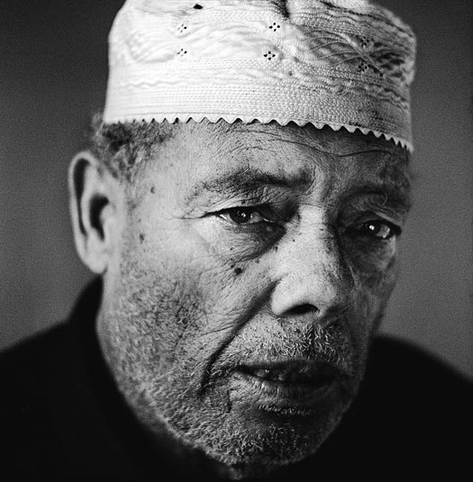An older man with a light beard, a square jaw, and a taqiyah on his head.