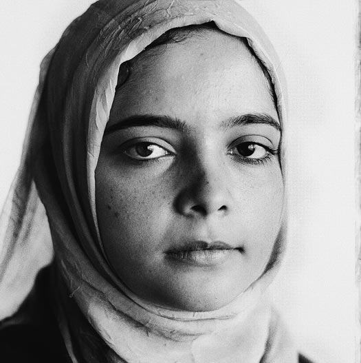 A girl, wrapped in a headscarf, with freckles and a round face.