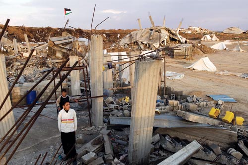 Two boys stand amidst rubble, with concrete pillars and rebar jutting up all around them.