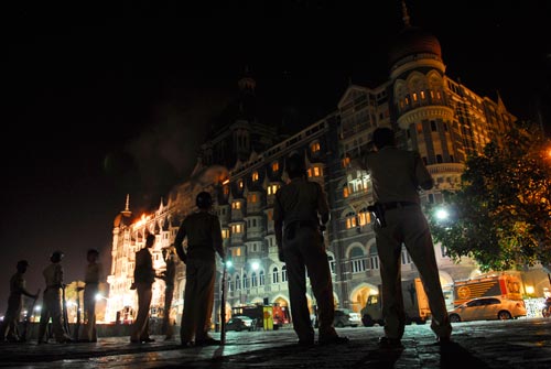 A line of khaki-wearing police officers stands a hundred yards back from an ornate, castle-like hotel. Smoke comes from one window, and it looks parts of the building are on fire.