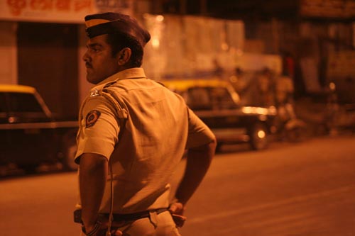 A police officer stands on the side of a street, hands on his hips.