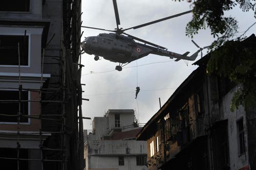 A man slides down a rope from a large helicopter onto the roof of a building.