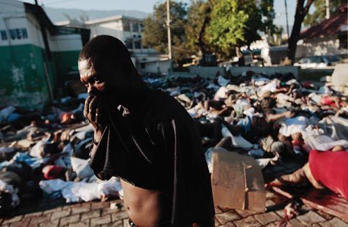 A brick plaza is covered with a tangle of bodies. A man walks by, holding his shirt up to cover his mouth and nose.