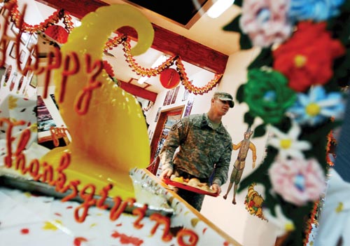 A man in a camouflaged uniform carries a food-laden tray down a hallway laden with Thanksgiving decorations.