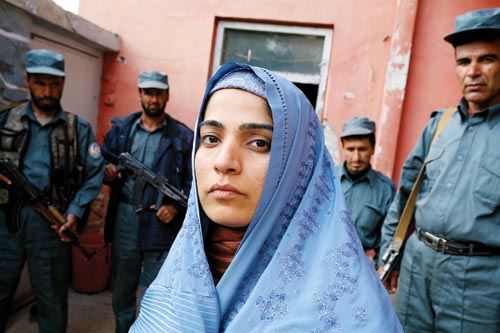 Clad in a sky-blue hijab, a young woman is flanked by four armed men.