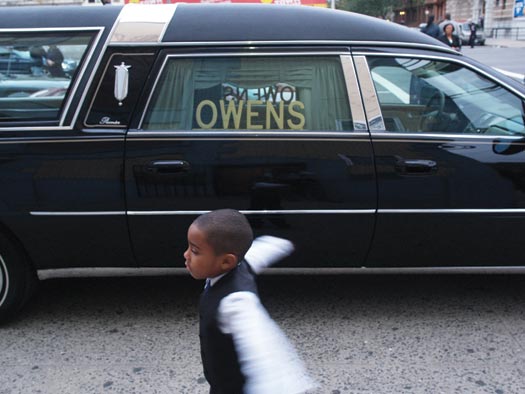 A formally dressed young boy plays while standing a few feet away from a Hearse.