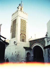 A four-sided minaret rises several stories above the whitewashed walls of a mosque.