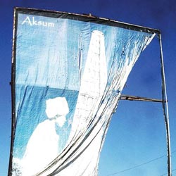 A weathered sign displays an obeslisk with a girl standing in front of it. The fabric of the sign has partially torn loose from its rusted frame.