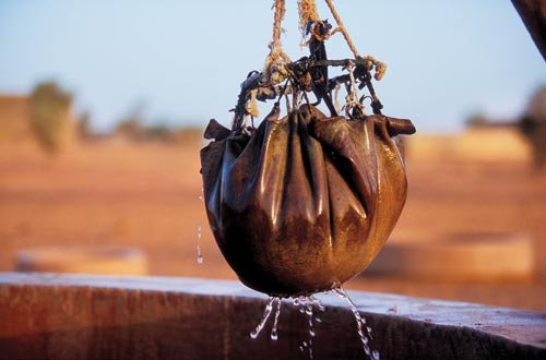 Suspended above an open well is a bag of water. A basketball-sized globe, it appears to be an animal skin, gathered together and fastened to a ring on top, with a rope used to haul it up.
