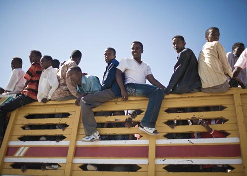 Dozens of boys crowd into the back of a truck, some packed like cattle within the bed's high sides, others riding up on the sides of the slatted walls.