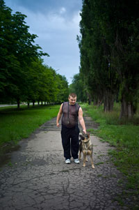 Oleg, a Zholtiy Vodi resident, walks his dog Kira down the cracked sidewalk across the street from the Electron-Gaz plant.