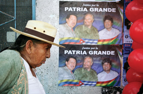 A woman walks past posters depicting Chávez, Bolivian president Evo Morales, and former Cuban president Fidel Castro.