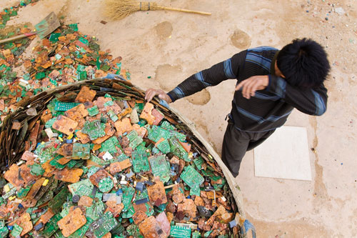A worker takes a brief break from sorting through stripped circuit boards in Guiyu, China.