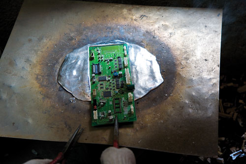 A worker melts the solder from a circuit board in order to harvest its microchips.