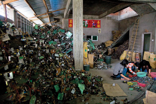Young women sort computer chips into plastic baskets in a small concrete and corrugated steel shack.