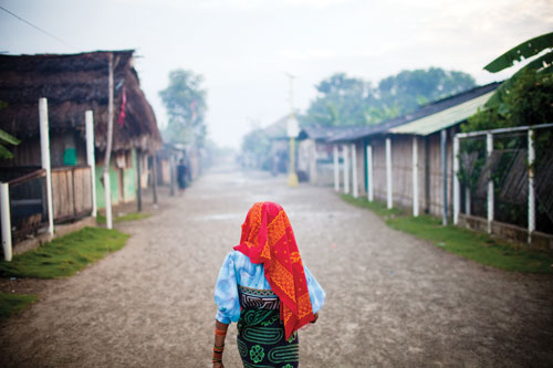 An elderly woman in traditional Kuna dress walks past Usdup island homes as the sun begins to rise.