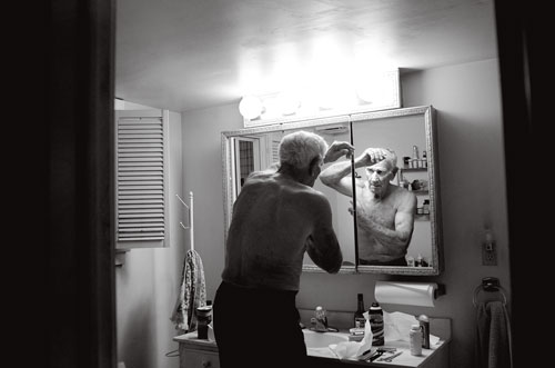 Tom looks at himself in the bathroom mirror while putting on deodorant after a day of working on the farm.