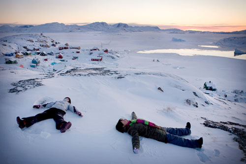 Children making angels in the snow on the hilltop of the tiny village of Aappilattoq, West Greenland.