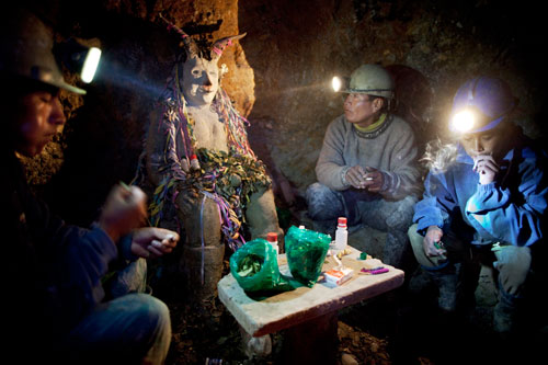 Miners Aurturo Seco, Alejandro Seco, and Milton Seco sit smoking cigarettes around a shrine to El Tio underground inside the mine.
