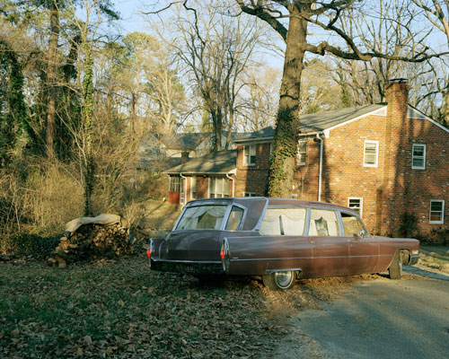 A brown hearse in the author's childhood driveway. The sun is setting and the ground is littered with leaves.