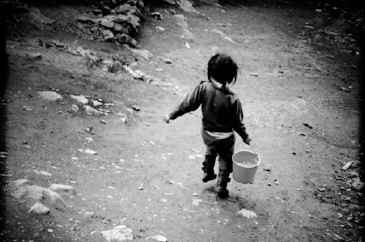 A girl lugs water, hoping to make a sale.