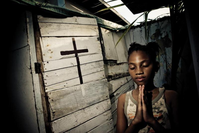 Annesha Taylor’s daughter prays at an altar constructed in their backyard in Arnett Gardens in Kingston.