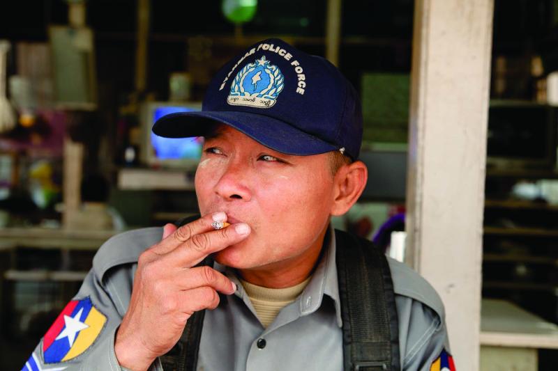 Sergeant Mg Mg Myint takes a drag at a riverside teashop in Tigyaing. The veteran police officer was quick to open his heart, and whiskey, to foreign guests. Photo by Jason Motlagh.