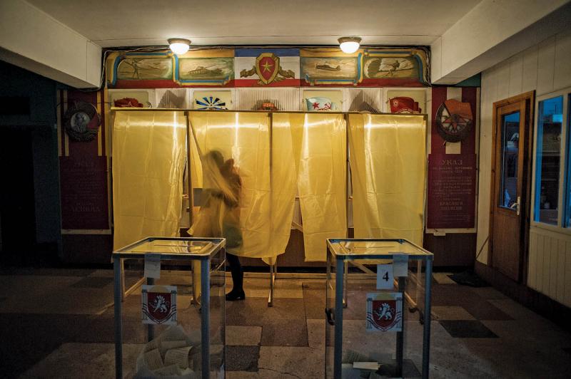 A voter at a polling station in Simferopol, March 16, 2014. On the wall behind the voting booth are various Soviet memorabilia, including the flag of the former Soviet Union and a portrait of Vladimir Lenin.