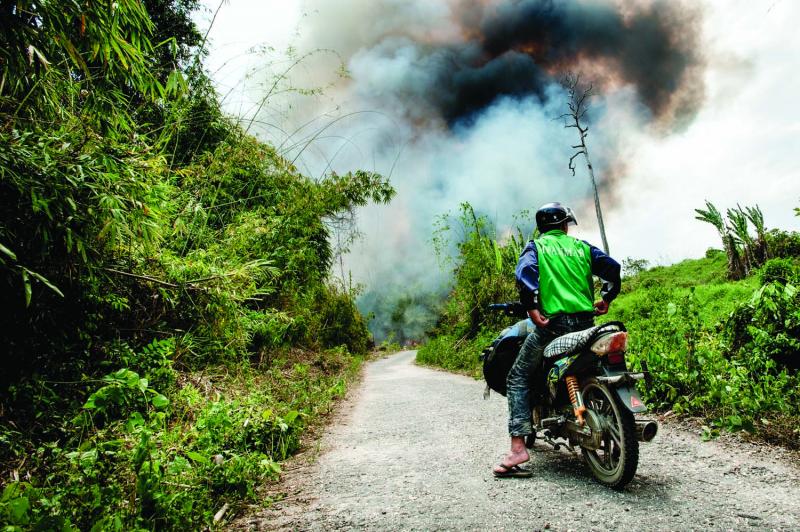 ￼A motorcycle driver waits as a controlled fire burns on both sides of the one-lane road that connects the Naga Hills to the busy Chindwin River watershed. The slash-and-burn method is still the most common form of cultivation in the jungles of northeast Myanmar.