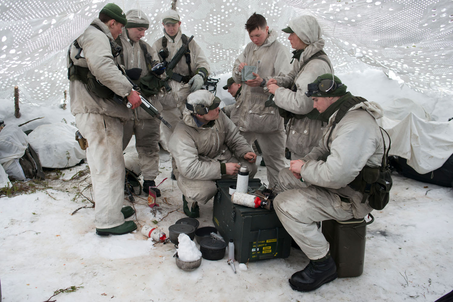 Swedish soldiers prepare food in a winter-camouflaged tent during military exercises. Norrbotten, Sweden, March, 2019.