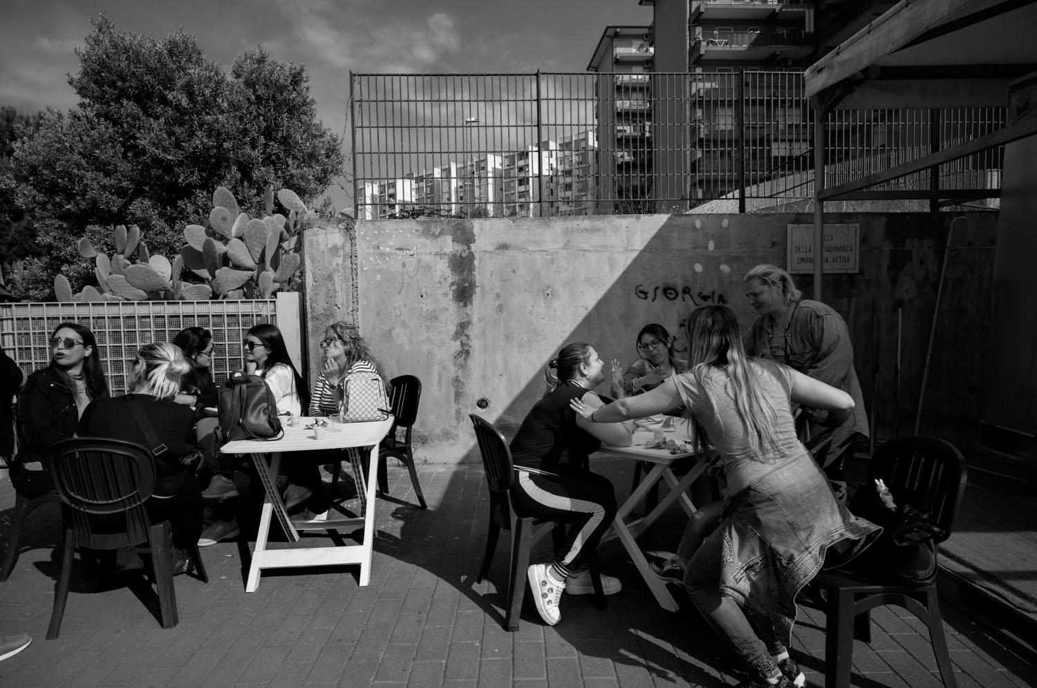 About 10 women socializing at outdoor tables. Librino, Sicily. May 2022.