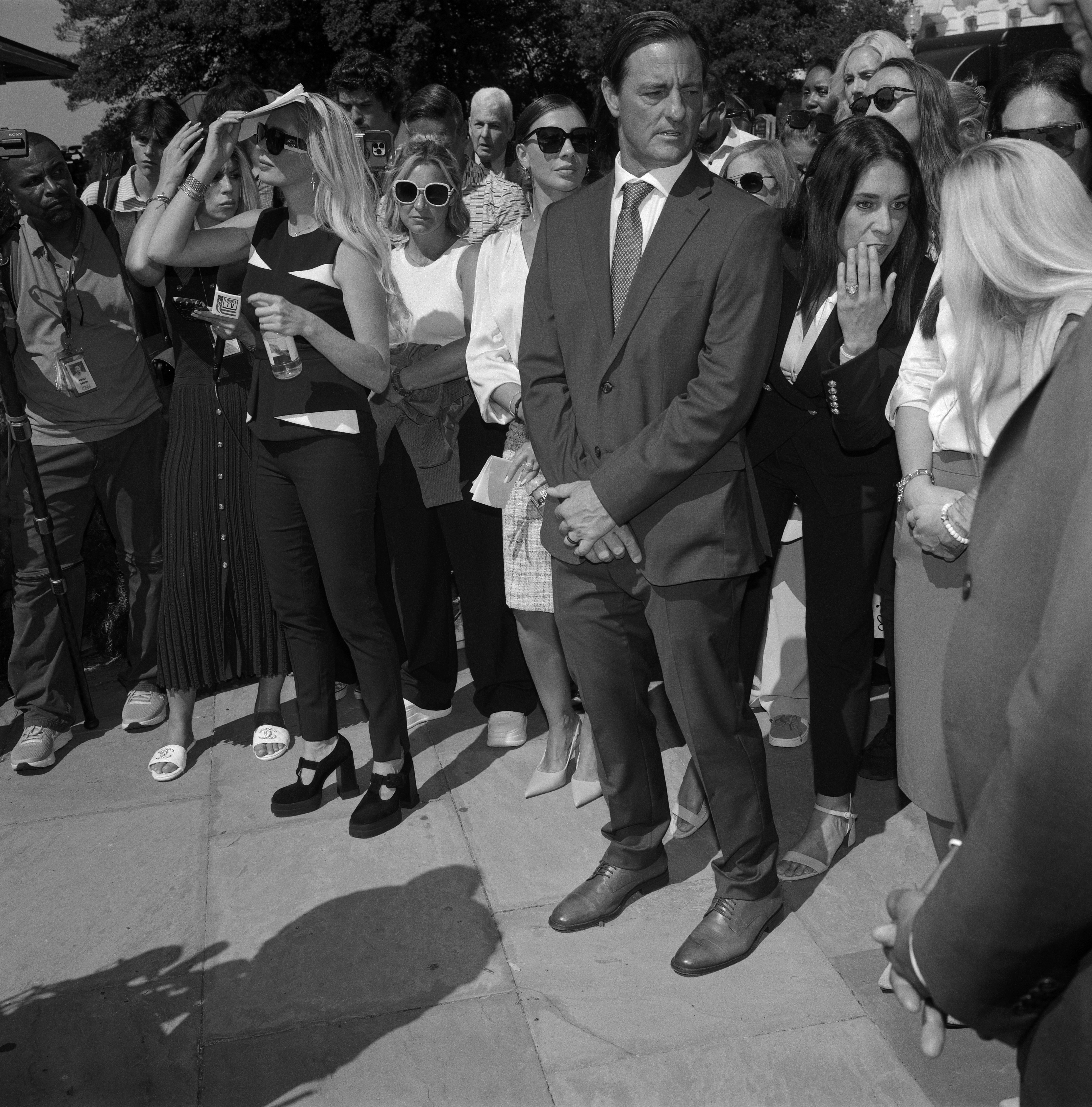 Two women whisper at outdoor press conference. 