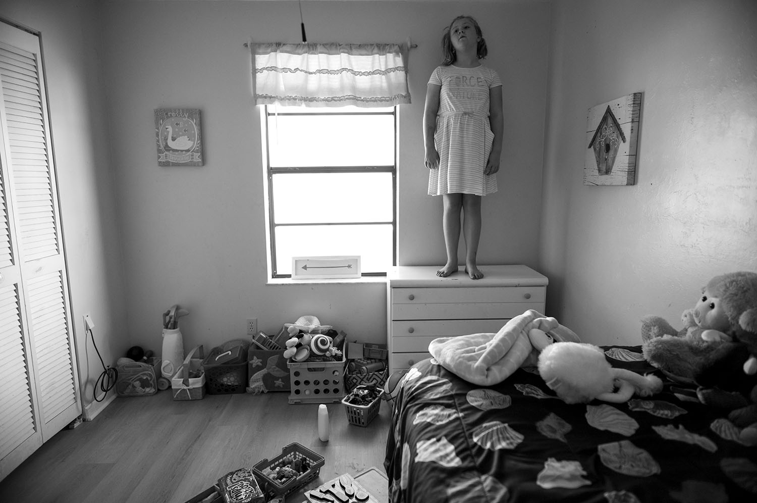 Girl stands atop dresser.