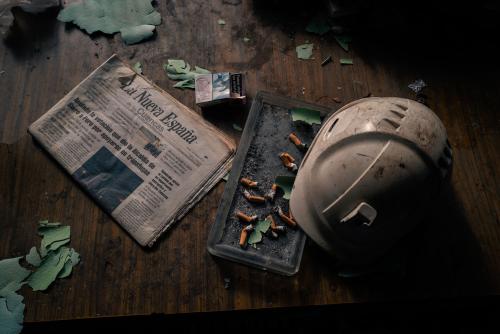 desk scene with a newspaper, hard hat, and ash tray with a dozen smoked cigarrettes