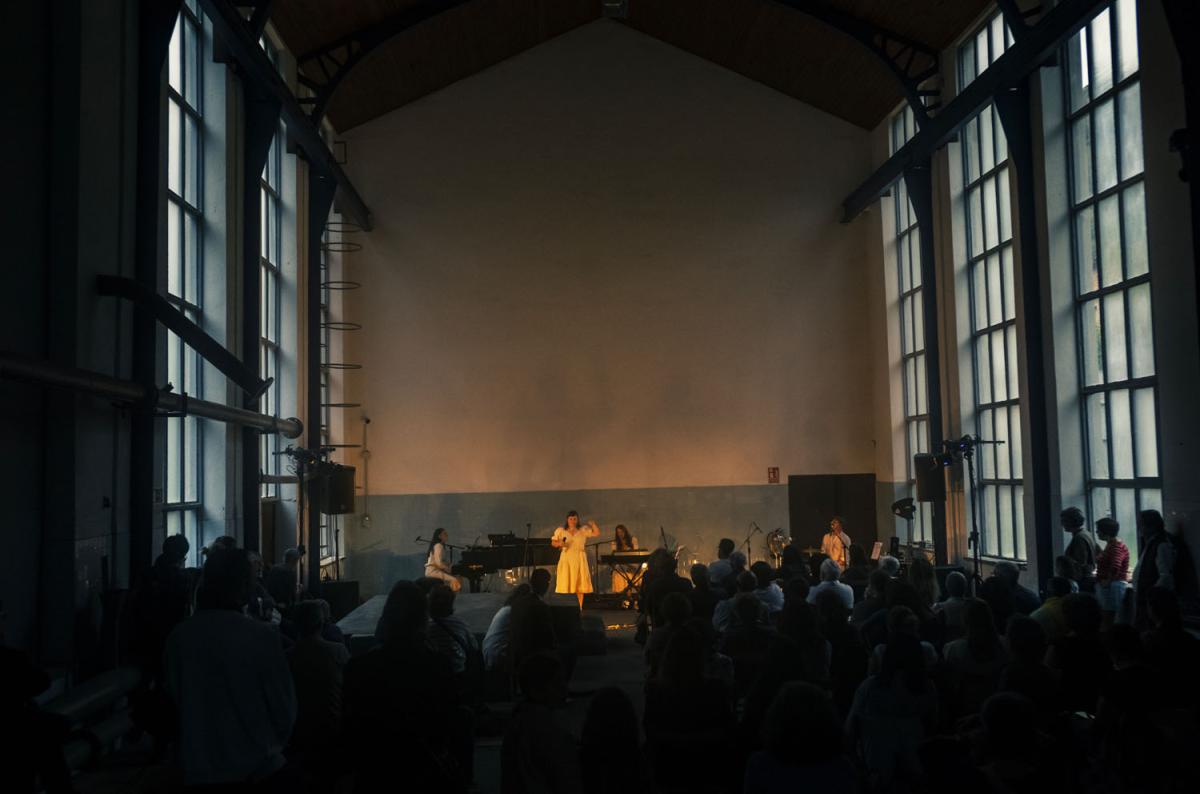 Woman on stage singing in a large hall with a high ceiling