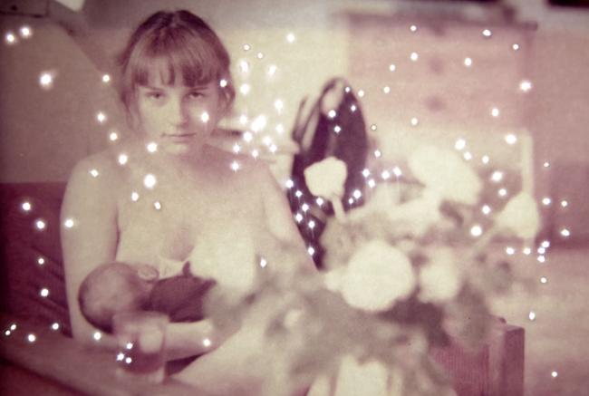 Photograph by Amy Friend of a baby being cradled by its mother. Photograph overlaid with small bright flash effects like stars or light on water.