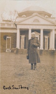 A white man with white hair stands in front of Thomas Jefferson's home. He is wearing an overcoat and holds a fedora in one gloved hand.